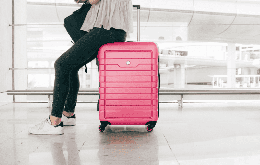 A women sitting on a pink suitcase in the airport