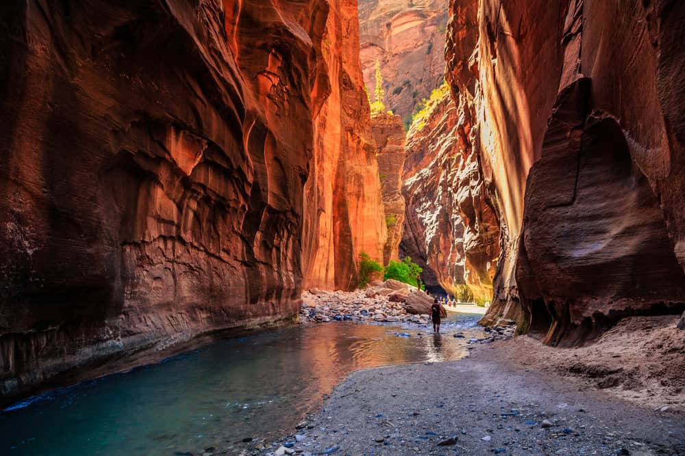 Hiker walking in water within rock formations on the Narrows Hike in Zion National Park 