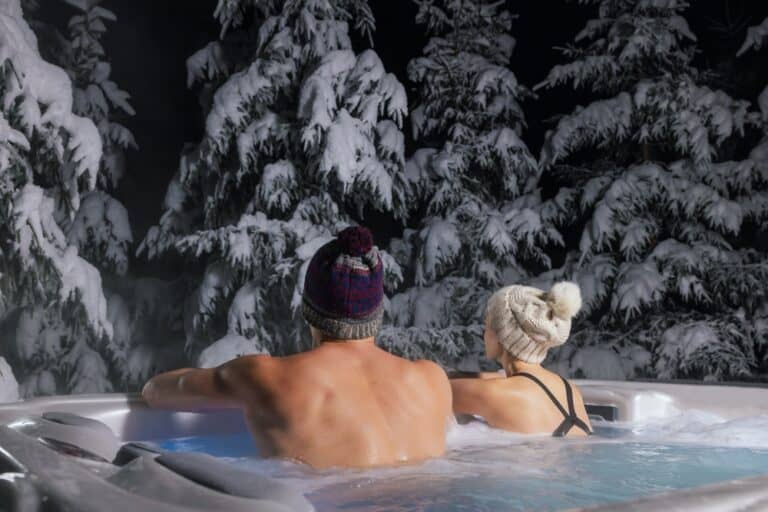 A couple relaxing in a hot tub looking at snow covered trees.