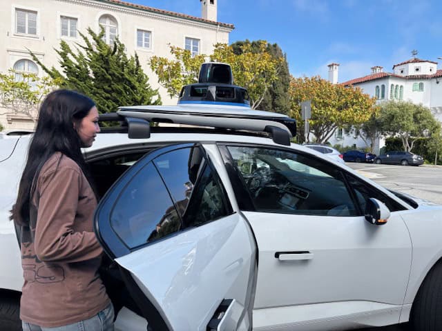 Girl getting into a white Waymo driverless car.